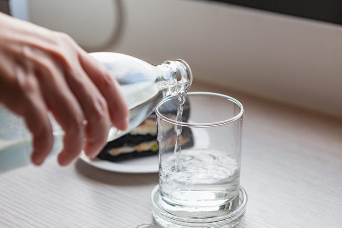 Drinking water is poured from a bottle into a glass on wooden table at office room.