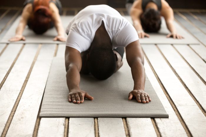 Young black man and group of young sporty people practicing yoga lesson with instructor, stretching in Child exercise, Balasana pose, working out, indoor, studio