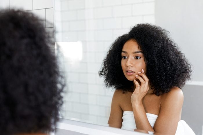 Woman looking in the bathroom mirror, touching her face