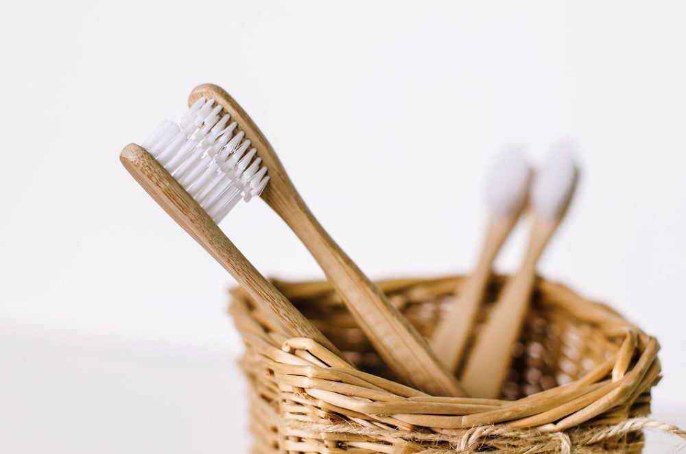 A family set of four wooden bamboo toothbrushes in a straw basket . Two toothbrushes are like parents in love kissing and in focus, and other two - are like children and blurred