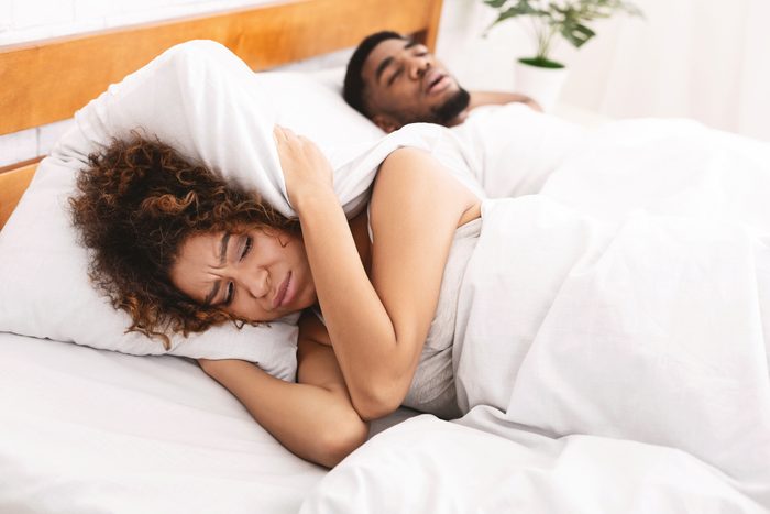 snoring man and woman covering ears with pillow