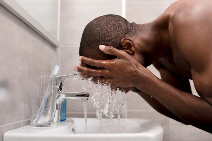 Man washing his face with water in a bathroom.