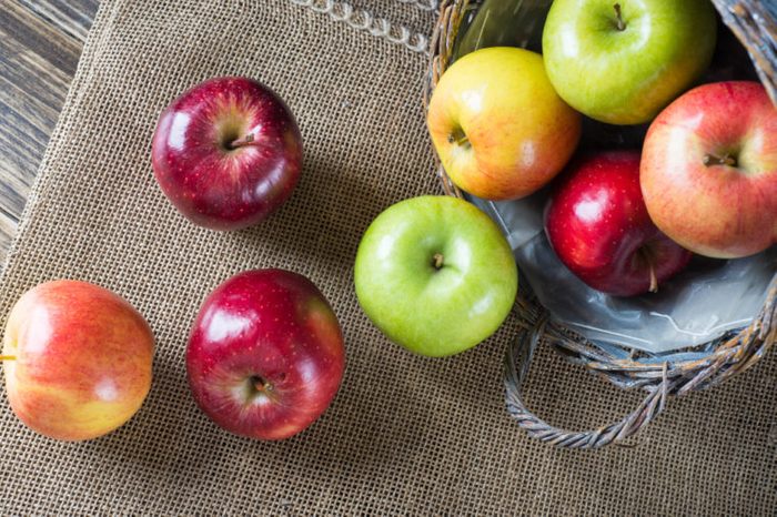 Apples in a basket on burlap and wooden background, view from the top