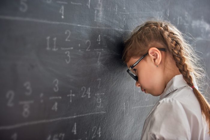 Tough day at school! Sad child near the blackboard indoors. Kid is learning in class. Complex math, arithmetic and examples. Numbers written with chalk on board.