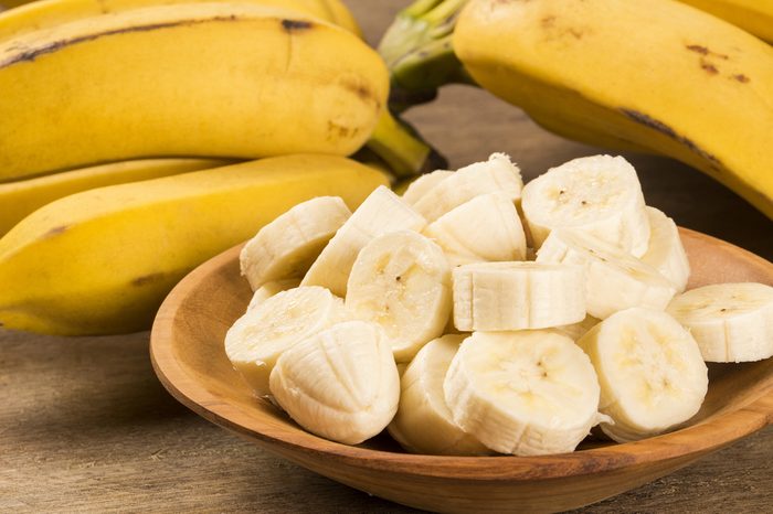 A bunch of bananas and a sliced banana in a bowl on a table.