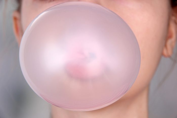 Person doing bubble with chewing gum on bright background