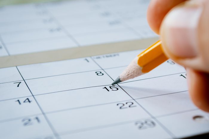 person writing in pencil on a calendar