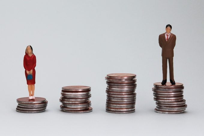 Gender wage difference concept. The miniature men and women are standing on the coin tower.