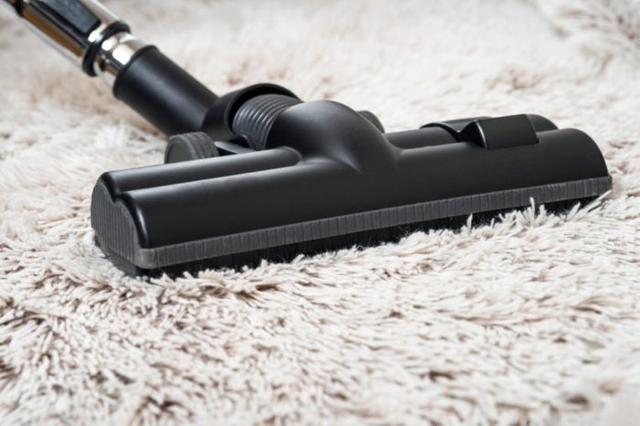 Close up of the head of a modern vacuum cleaner being used while vacuuming a thick pile white carpet
