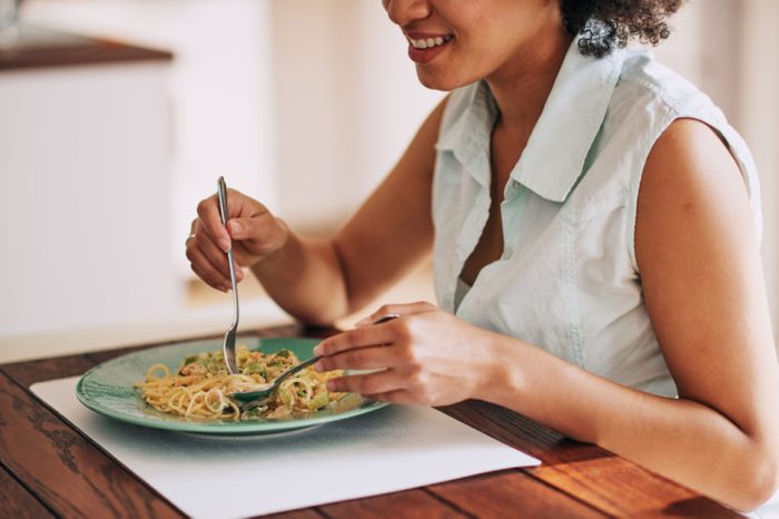 Woman eating plate of pasta at table