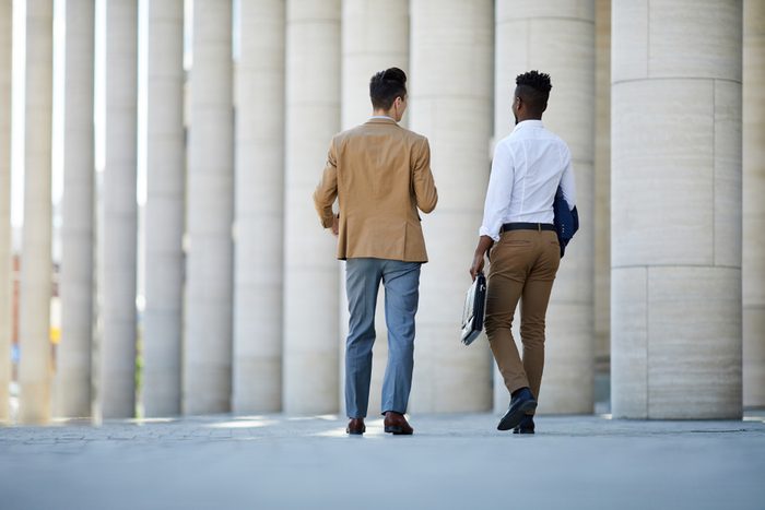 Two young intercultural businessmen in formalwear walking to work while having talk