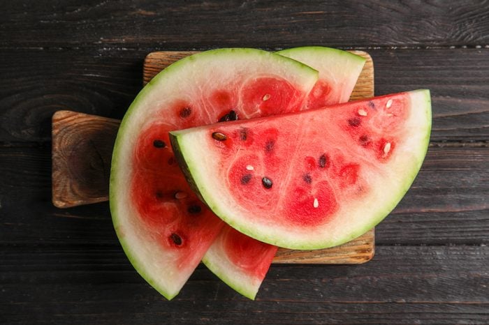 Board with juicy watermelon slices on wooden background, top view