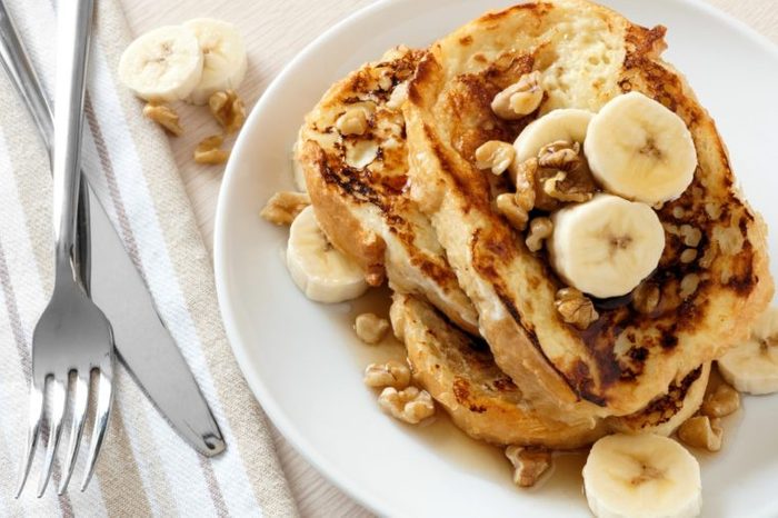 Plate of delicious French toast with bananas, walnuts and dripping maple syrup.