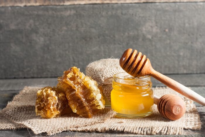 Glass jar of honey surrounded by honeycomb