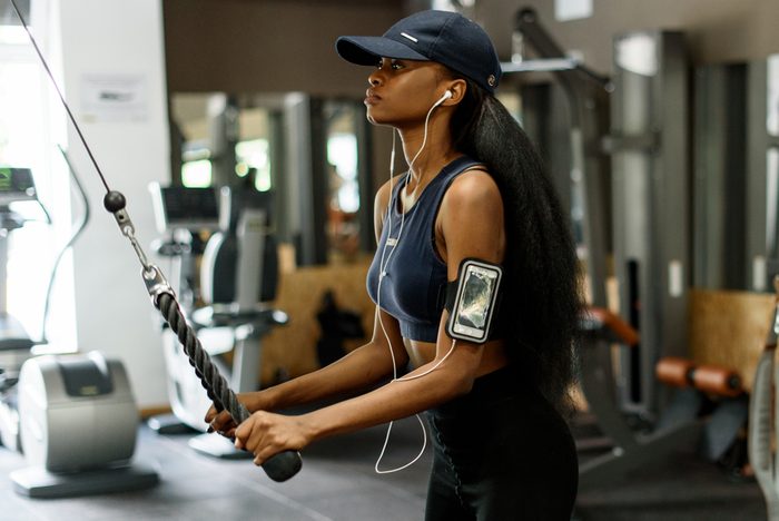 Side view of sexy gorgeous african-american woman working out at the gym and listens to music in white earphones