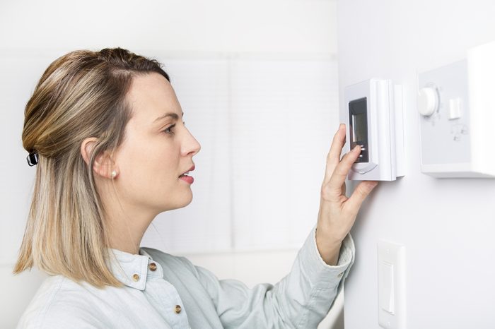 A woman setting the thermostat at a house