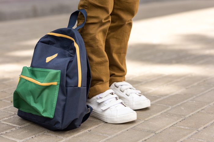 cropped shot of stylish schoolboy standing with backpack on street