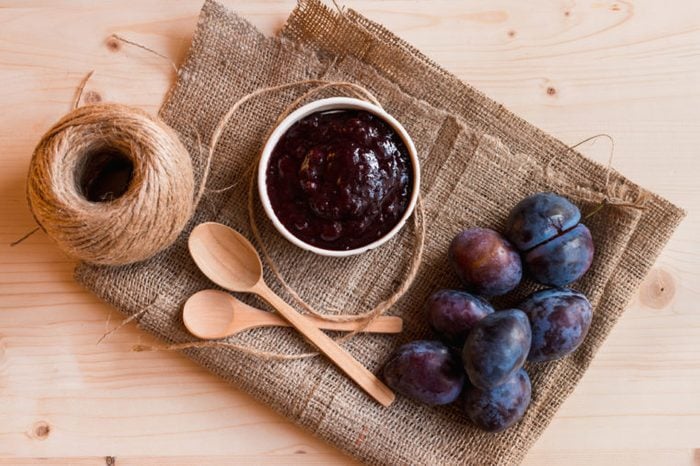 Bowl of plum jam and raw plums on burlap cloth
