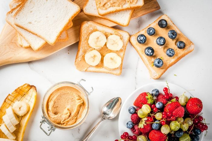 Traditional summer breakfast: sandwiches of toast with peanut butter, berry, fruit apple, peach, blueberry, blueberry, strawberry, banana on a white marble table. 