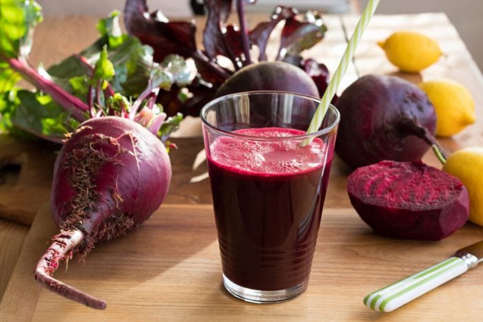 Glass of red beet juice in front of raw beets and lemons