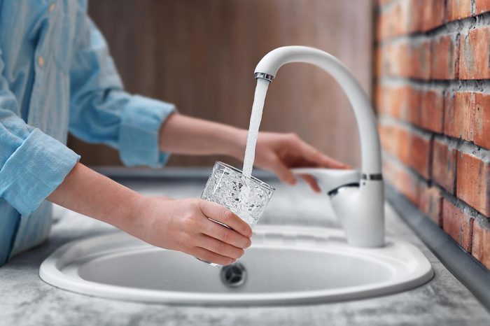 woman filling glass of water at faucet