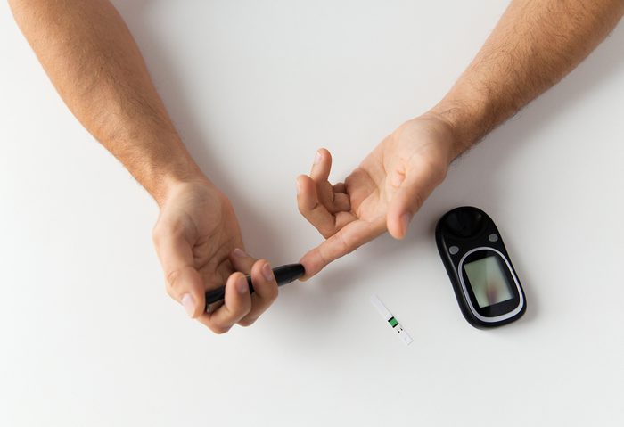medicine, diabetes, glycemia, health care and people concept - close up of man checking blood sugar level by glucometer at home