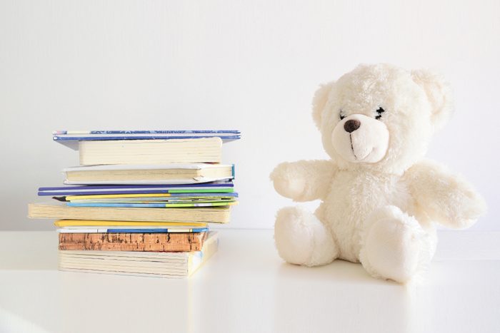Some books in a pile and a teddy bear on it. Bookshelf in a child bedroom. Empty copy space for Editor's text.