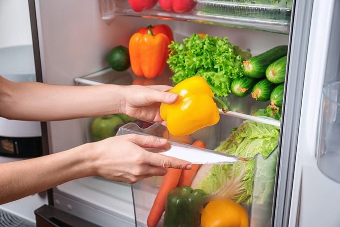 Young woman taking fresh pepper from refrigerator