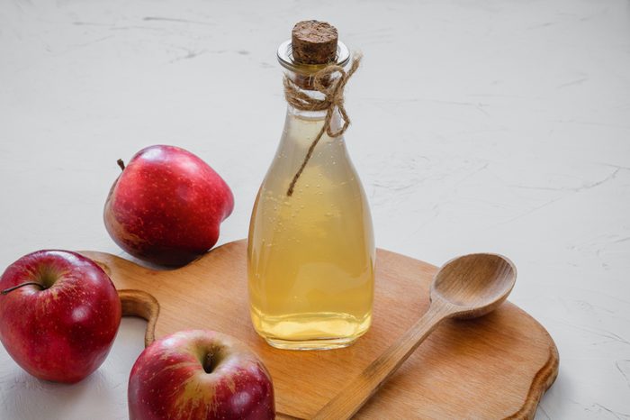 bottle of apple cider vinegar and wooden spoon on wooden board, three apples