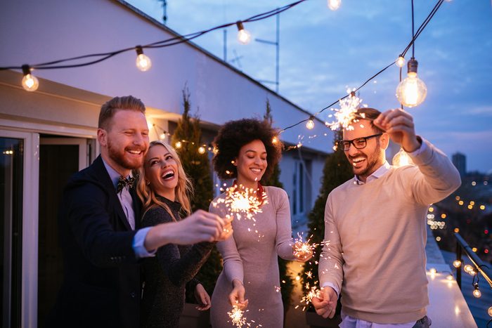 Friends enjoying a rooftop party and dancing with sparklers in hands.