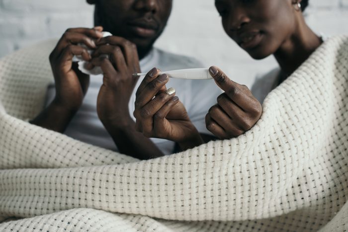 cropped shot of young african american couple checking thermometer while having flu together