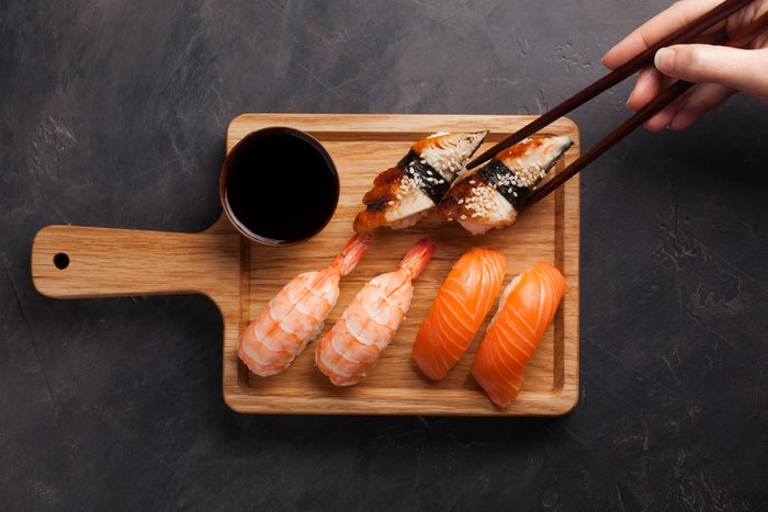 A set of sushi with salmon, shrimp and eel and wooden chopsticks on a wooden Board. Delicious Japanese food on a dark stone background. female hand takes the chopsticks in the sushi. Top view.