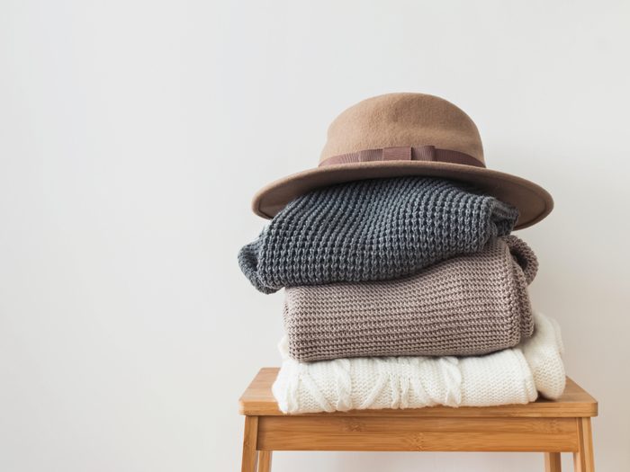 Stack of warm knitted sweater and felt hat on the top of it at the white wall background.