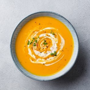 Pumpkin and carrot soup with cream on grey stone background. Top view.