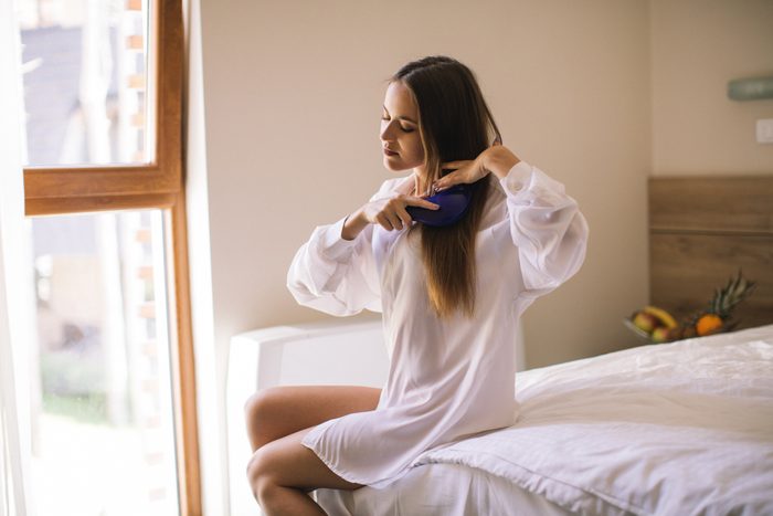 woman sitting on edge of bed brushing her hair
