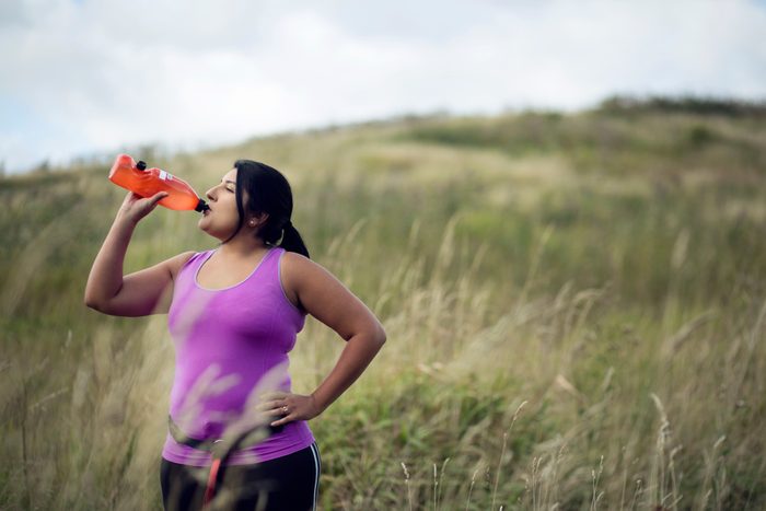 young woman drinking water while exercising outside