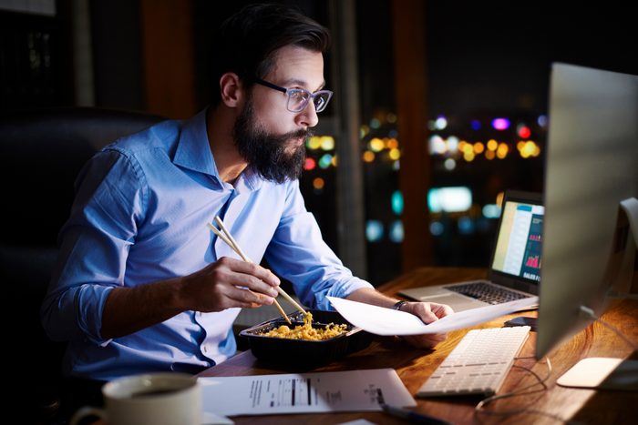 man eating dinner at night while working