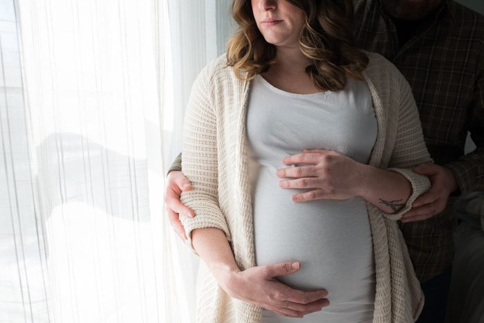 pregnant woman touching belly with husband standing behind her