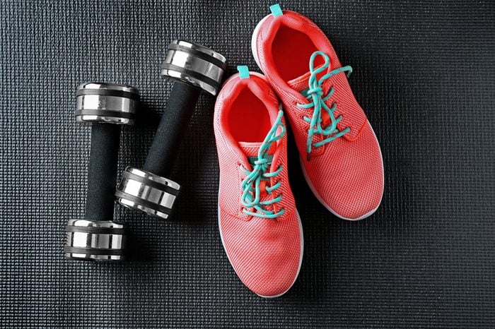 Pink running shoes and black dumbbells on dark background.
