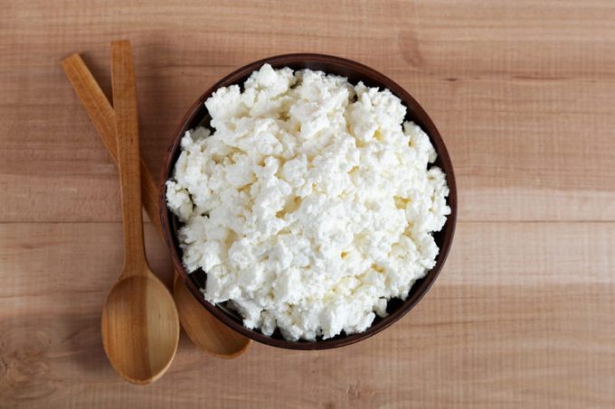 Fresh cottage cheese in a bowl with spoon on a wooden table.