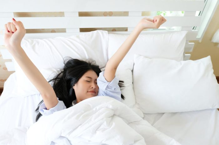 Top view of smiling asian woman waking up after sleep and stretching on bed .Beauty and relaxation concept.