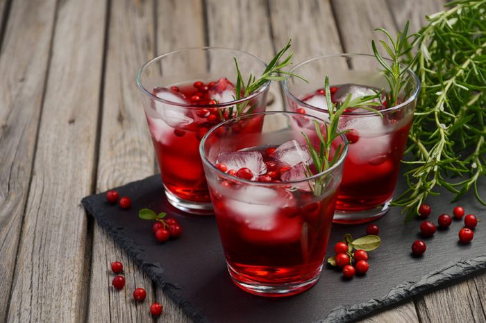 Three glasses of cranberry juice with ice displayed with rosemary on wooden background