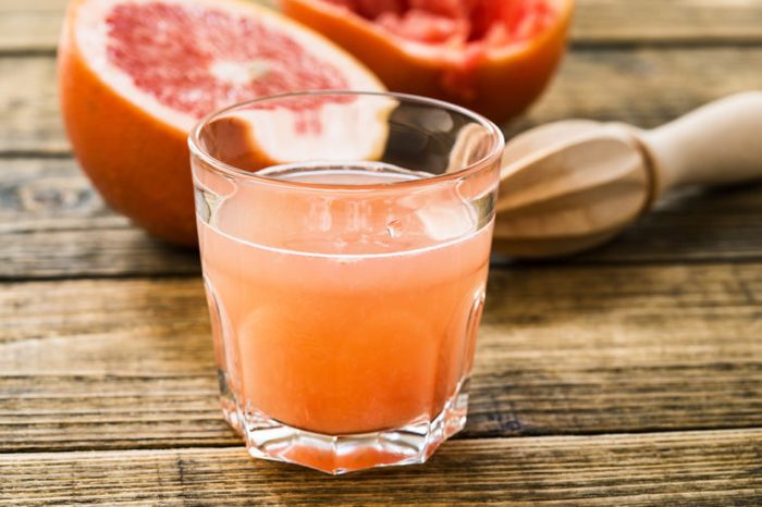 Glass of fresh organic pink grapefruit juice ready to drink and two pink-grapefruit halves