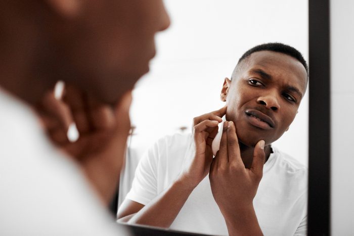 man looking at pimple in mirror