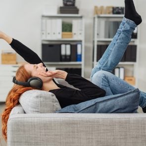 Exuberant young woman listening to music as she relaxes on a sofa laughing and kicking her legs and arms