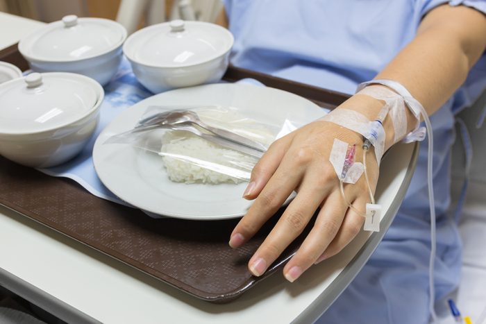 Asian Pregnant Woman patient is on drip receiving a saline solution with cooked rice and other food in white bowl , selective focus.