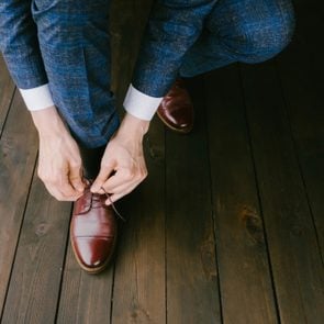 Man wearing a blue suit putting his brown shoes on. Hands and shoe close-up