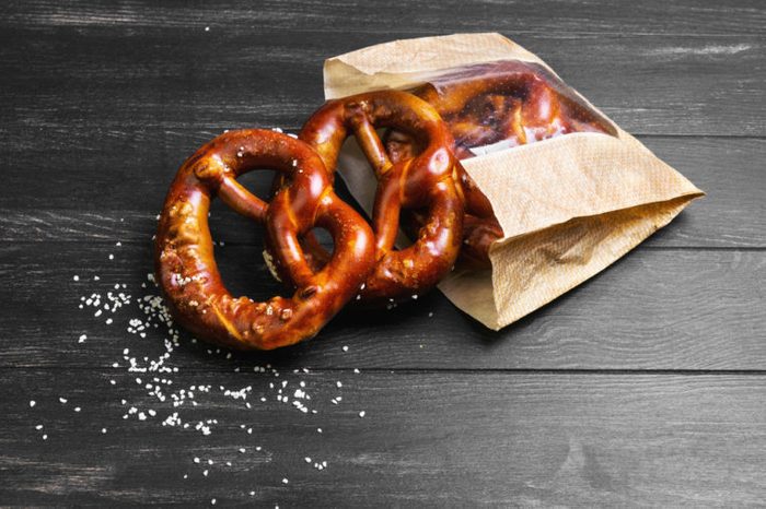 Fresh German pretzels with sea salt close-up, paper packaging for pretzels on dark black board background