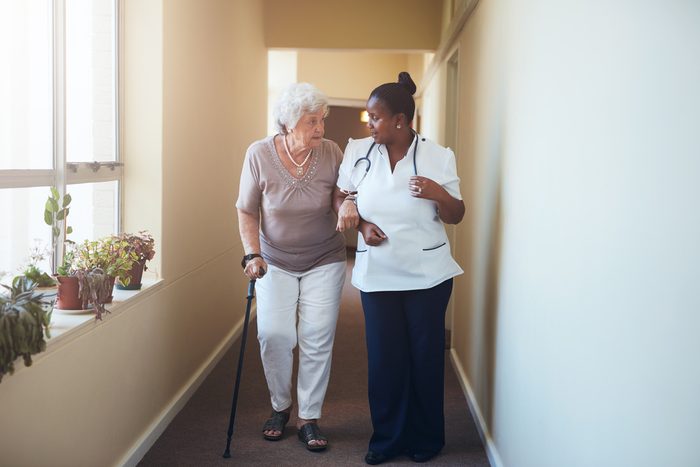 Senior woman with walking stick being helped by a female nurse at home. Full length shot of female doctor with elderly patient at nursing home.