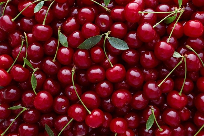 Close up of pile of ripe cherries with stalks and leaves. 